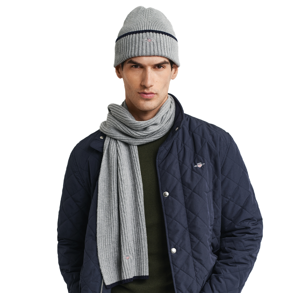 Man wearing a navy quilted jacket, gray beanie, and scarf on a white background