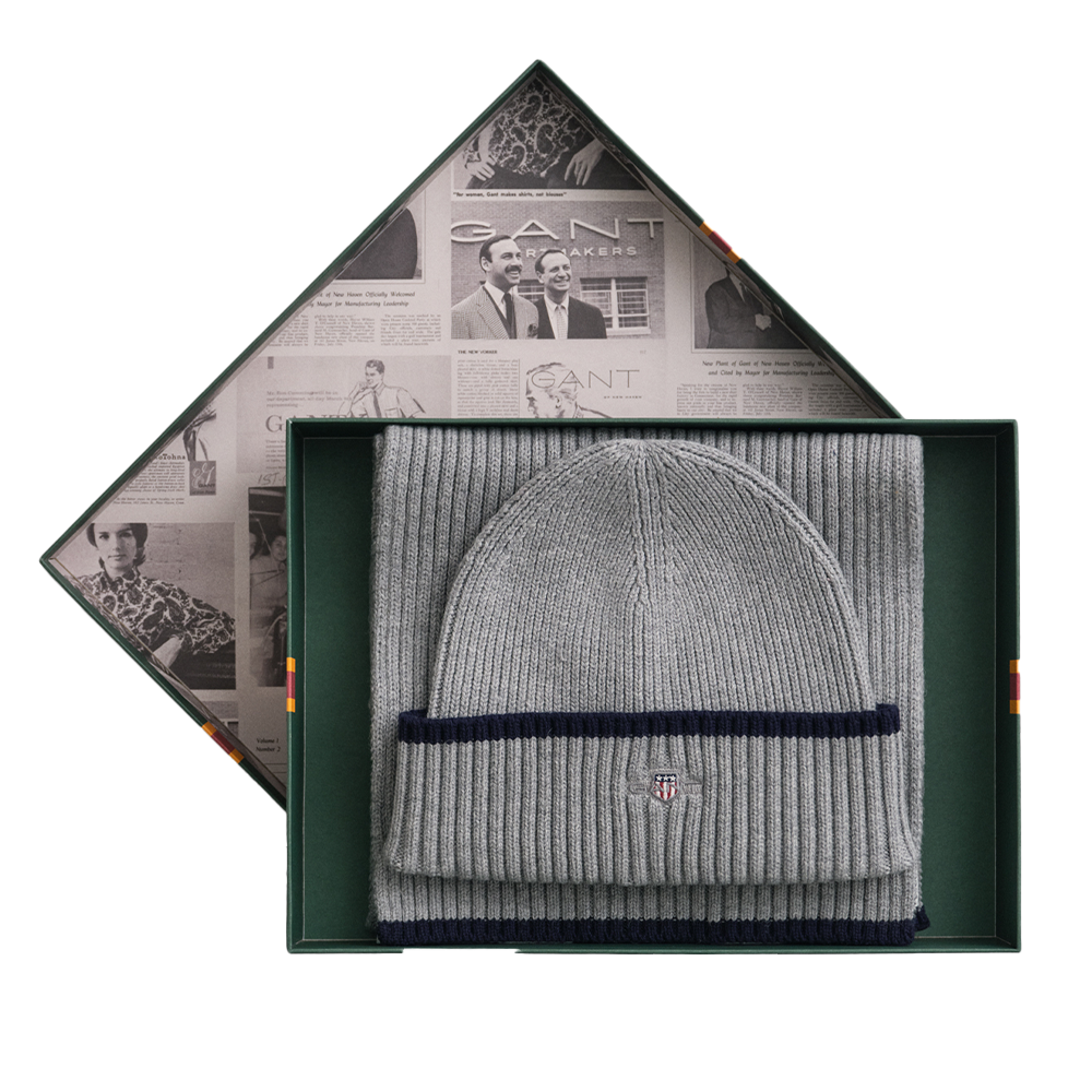 Gray beanie with navy band in a decorative box with newspaper design