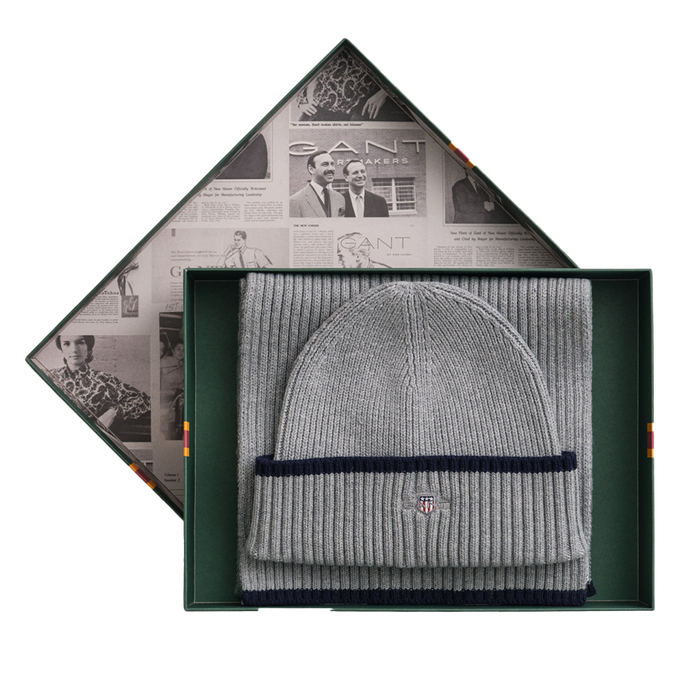 Gray beanie with navy band in a decorative box with newspaper design