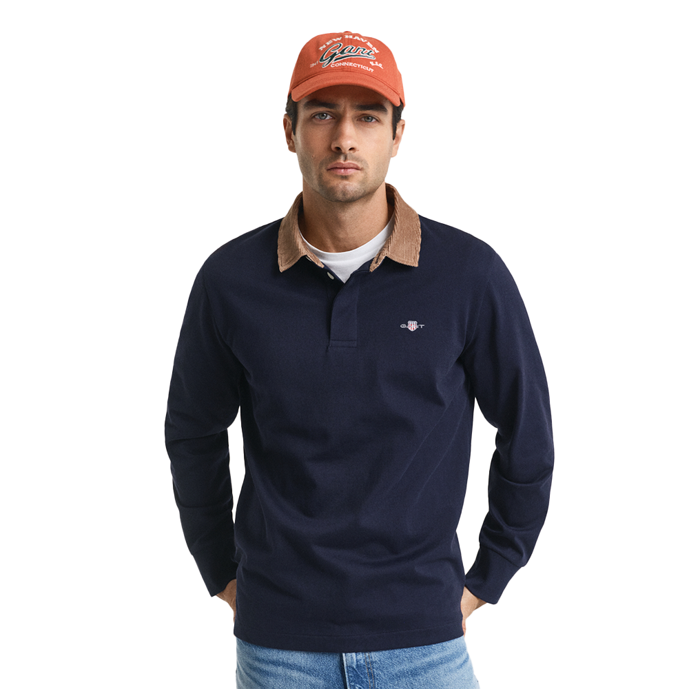 Man wearing a navy long-sleeve polo shirt with a brown collar, orange cap, and blue jeans on a white background.