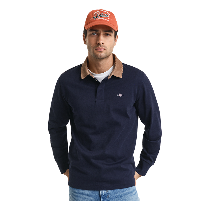 Man wearing a navy long-sleeve polo shirt with a brown collar, orange cap, and blue jeans on a white background.