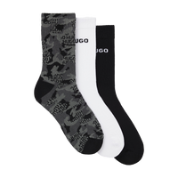 Three pairs of socks in gray camouflage, white, and black with 'HUGO' branding on a white background.