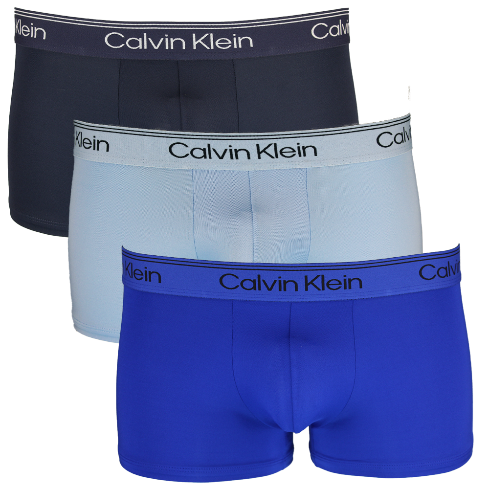 Three pairs of Calvin Klein boxer trunks in navy, light blue, and blue on a white background.