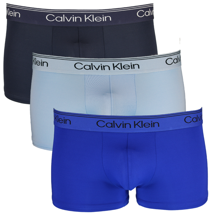 Three pairs of Calvin Klein boxer trunks in navy, light blue, and blue on a white background.